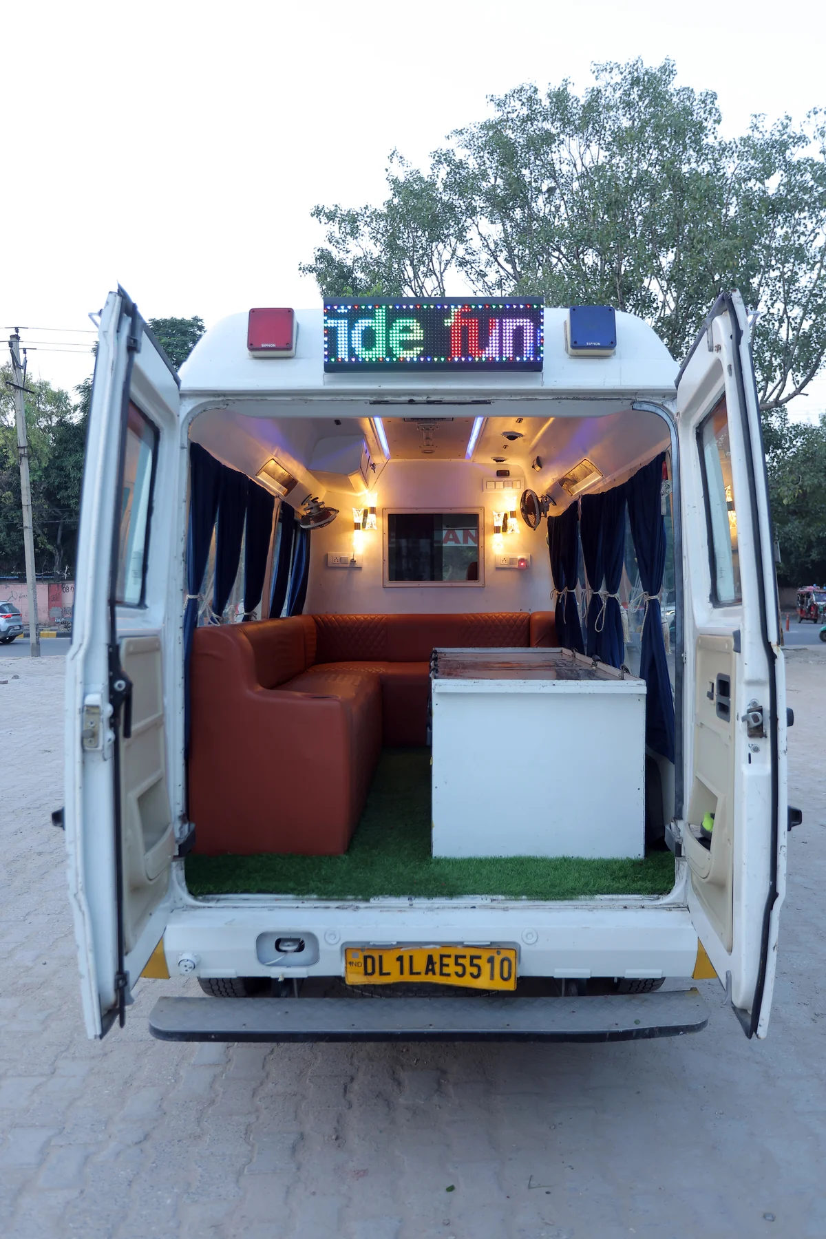 Interior of Last Ride Funeral premium glass hearse van showing orange upholstered family bench seating, central casket platform with astroturf lining, LED FUNERAL scrolling signage and ambient interior lighting — Delhi NCR