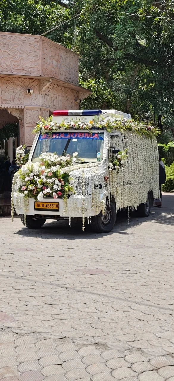 Last Ride Funeral premium hearse van decorated with cascading jasmine garlands and floral arrangements arriving at a Delhi shamshan ghat gateway for the Antim Sanskar