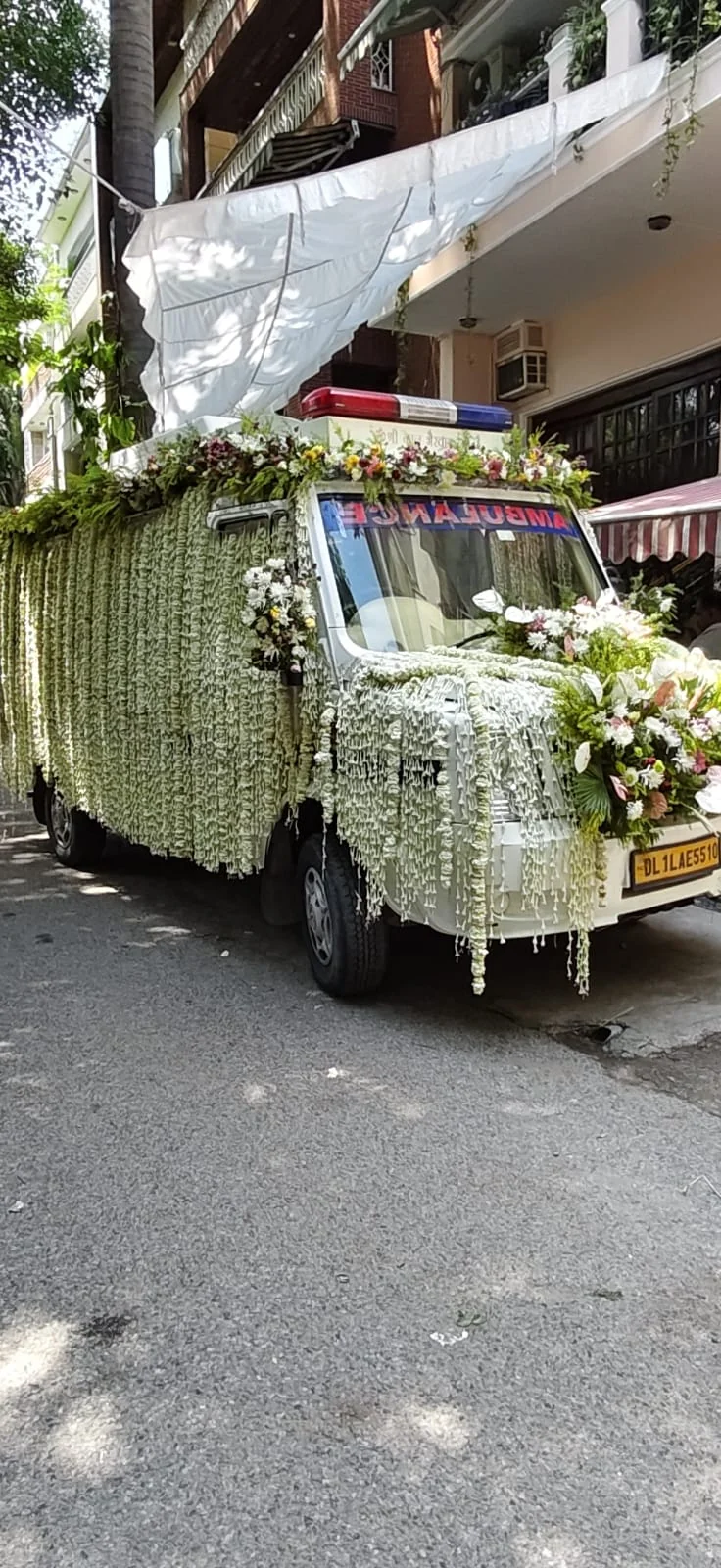 Last Ride Funeral premium hearse van covered in cascading jasmine garlands with pink rose and white chrysanthemum bouquets, parked outside a Delhi residence for home pickup before the Antim Yatra